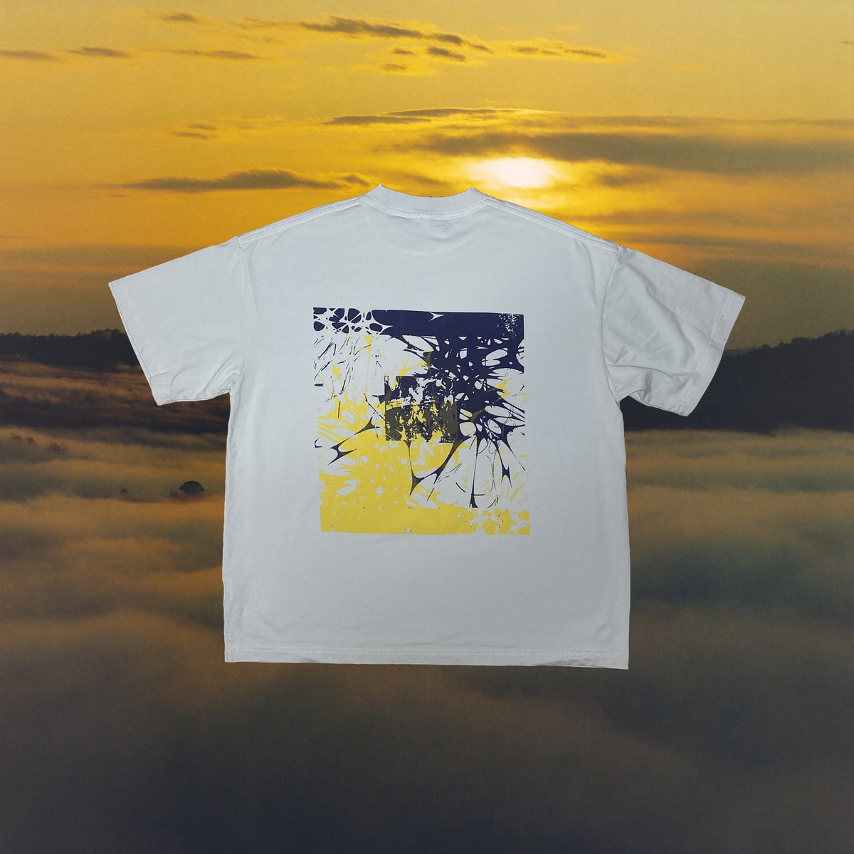 Sage tee with yellow and navy shattered glass back print, golden sunset backdrop